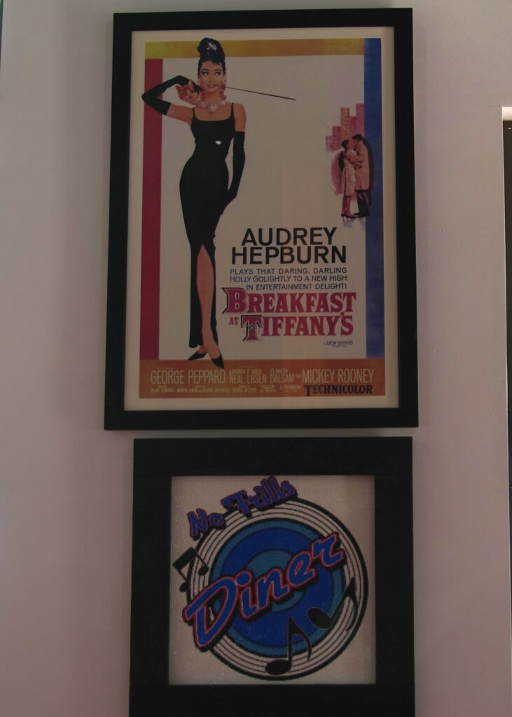 Wall poster of Audrey Hepburn for her movie "Breakfast at Tiffany's" with a smaller "No Frills Diner" framed picture below it.